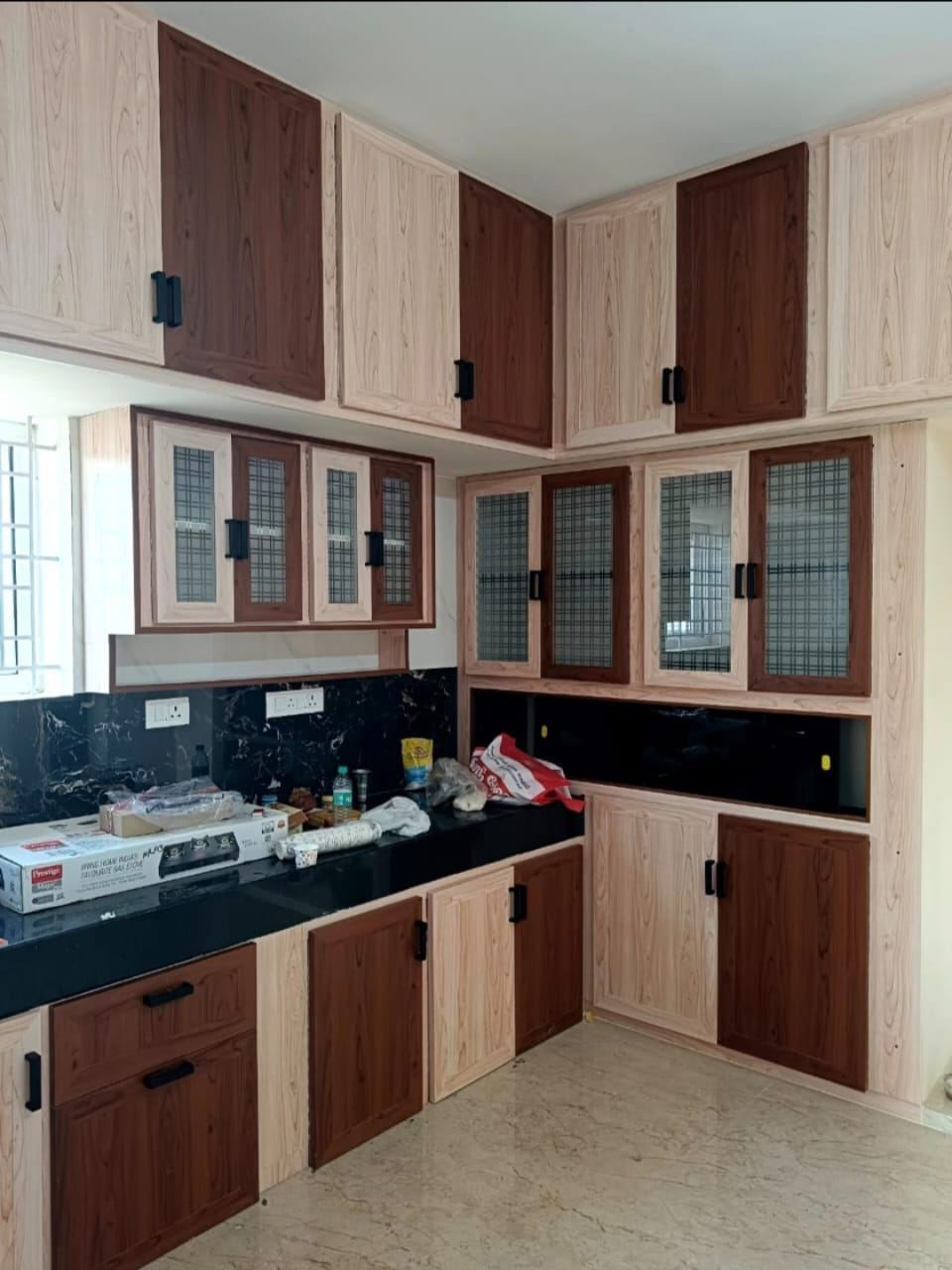 Dual-tone walnut and cream PVC/uPVC modular kitchen with glass-front wall cabinets and black granite countertop